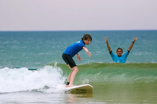Jeune surfeur prenant une vague verte pendant que son moniteur célèbre dans l'eau derrière lui à Hossegor