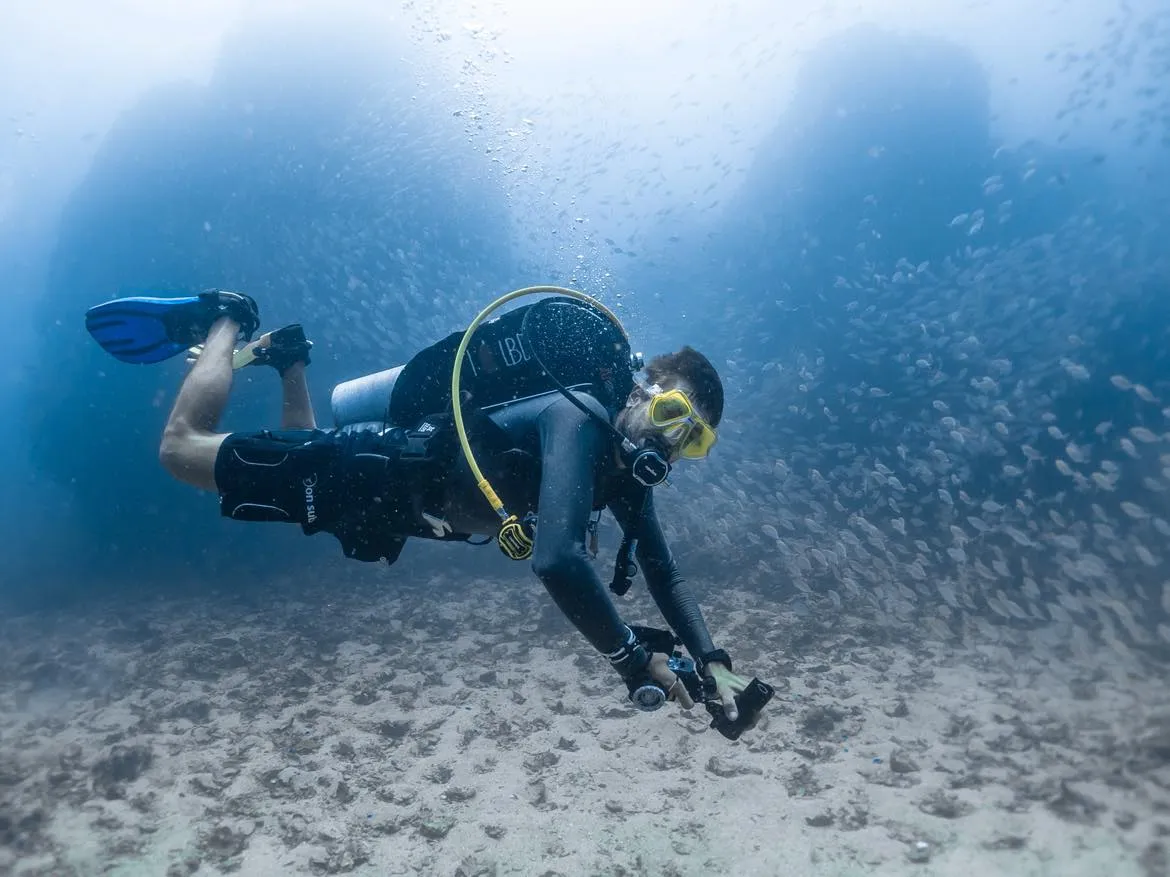 Scuba diver swimming among a school of fish in deep blue water off Menorca