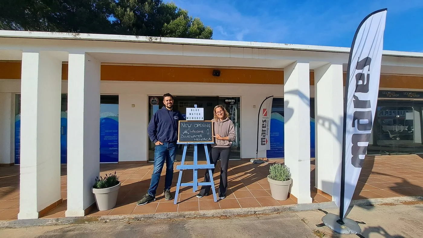Vooringang van duikcentrum Blue Water Menorca met welkomstbord en Mares-vlag