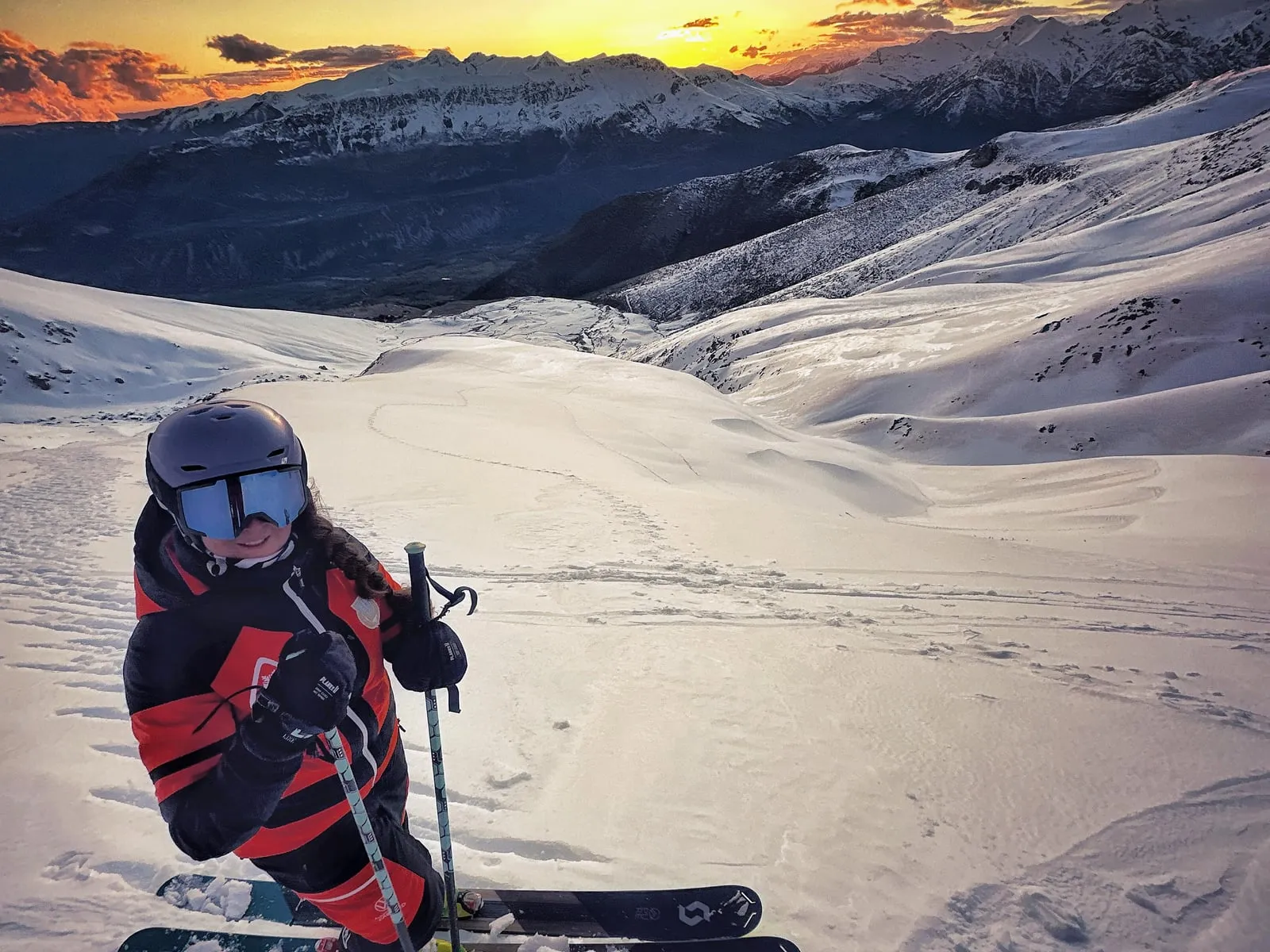 A skier stopped on the slope at sunset, the peaks of the Pyrenees lit orange behind