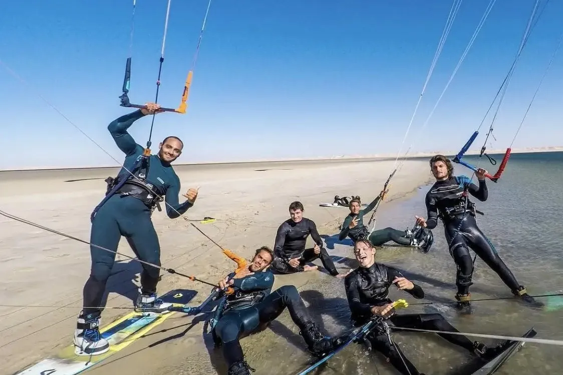 A group of Seb Garat Ride Academy kitesurfers smiling together in a shallow lagoon with their kites overhead