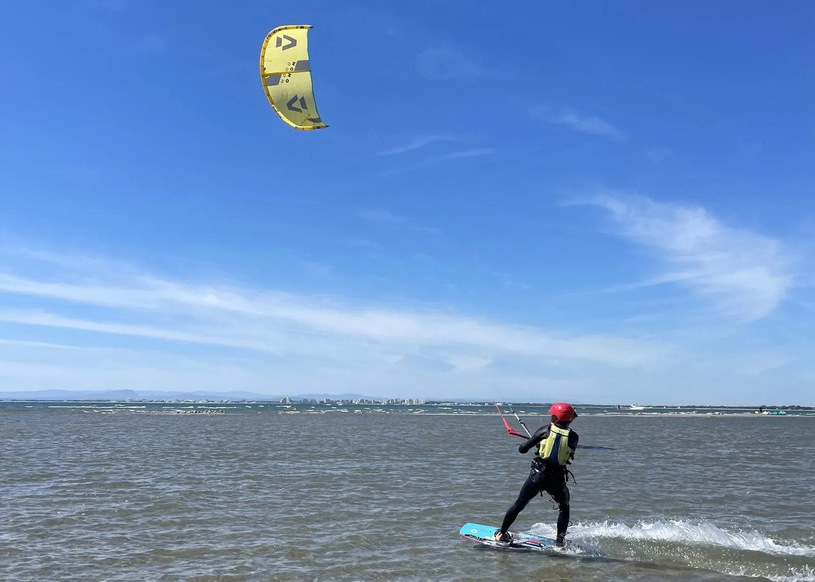 A Seb Garat Ride Academy rider gliding across shallow clear water under a yellow kite