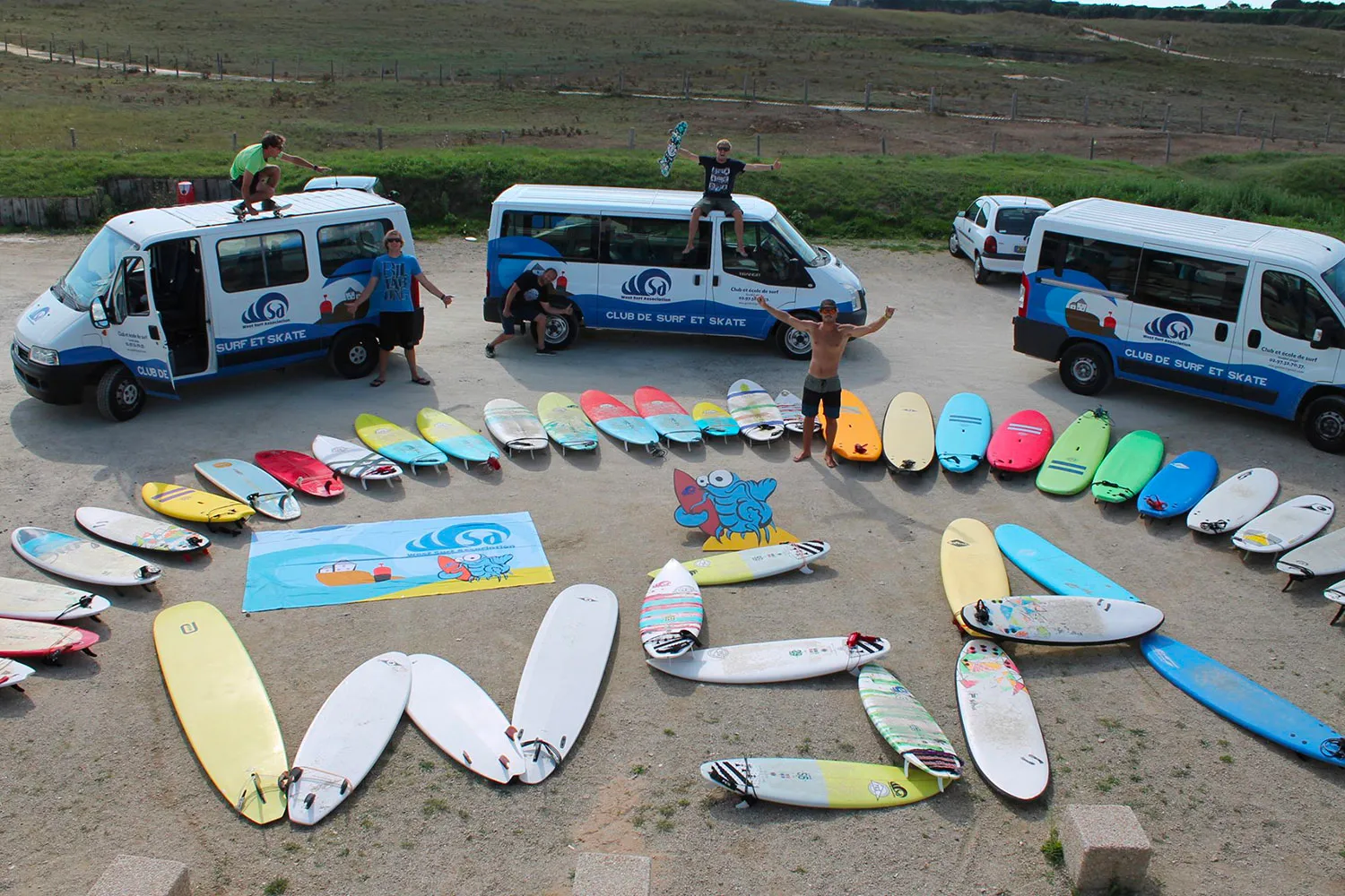 WSA Guidel surf school fleet of colorful surfboards arranged around branded vans