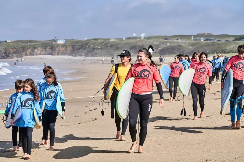 WSA Guidel surf students in branded rash guards walking along the beach with surfboards