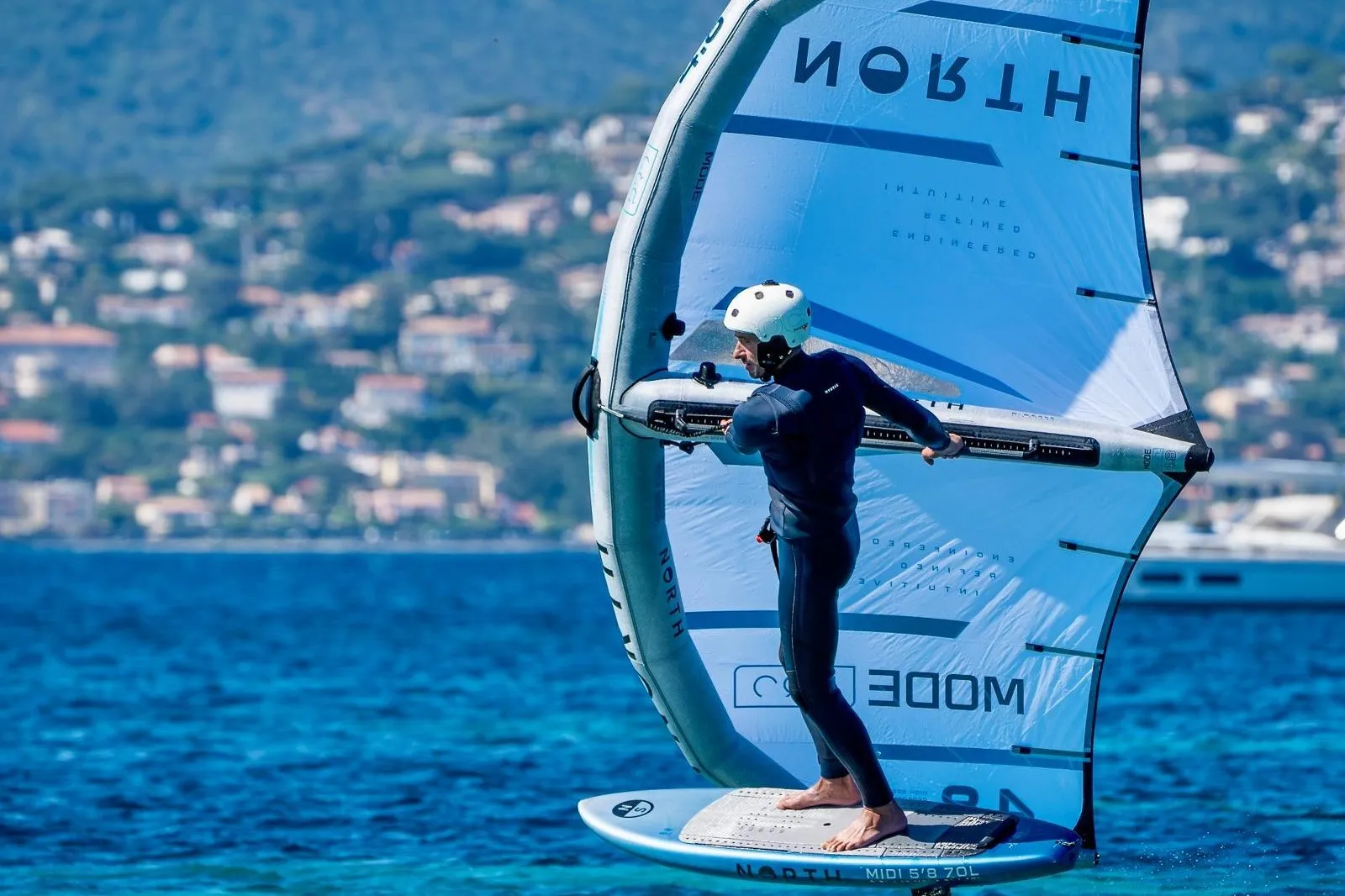 Wing foiler gliding across the turquoise bay of Saint-Tropez, hillside villas and a yacht in the background