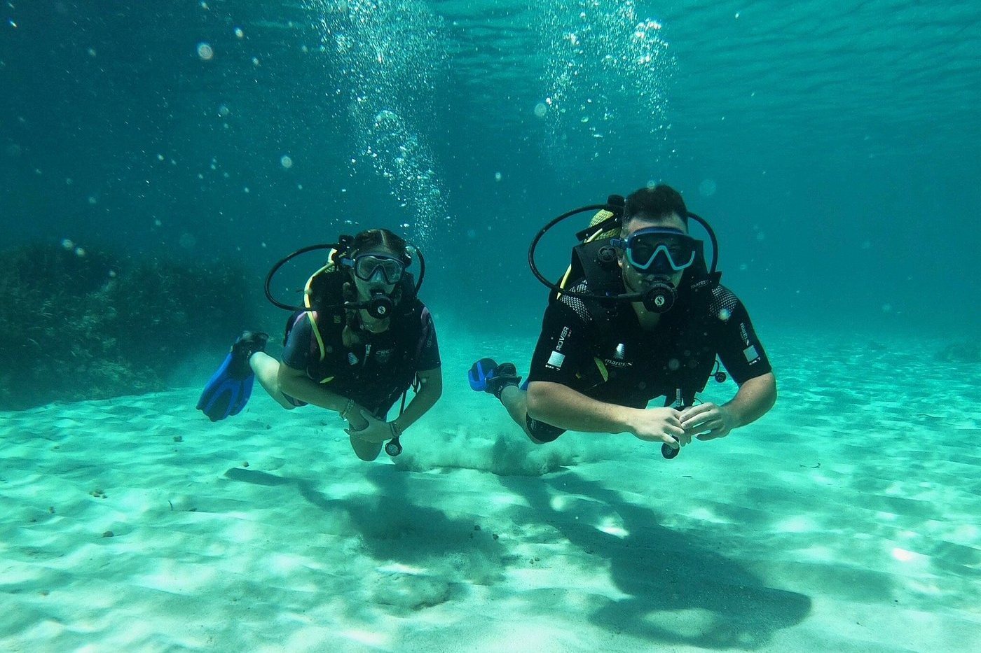 Two scuba divers exploring the sandy seabed in clear turquoise waters off Menorca