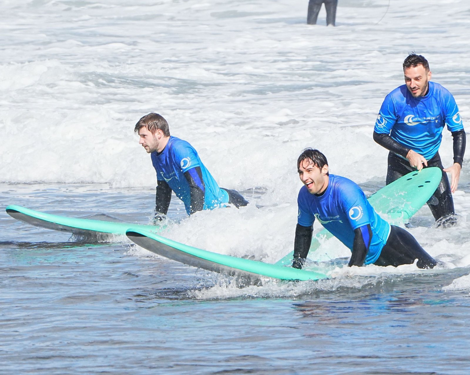 Tre allievi di Azores Surf Center scivolano sorridenti sulla schiuma con le loro tavole