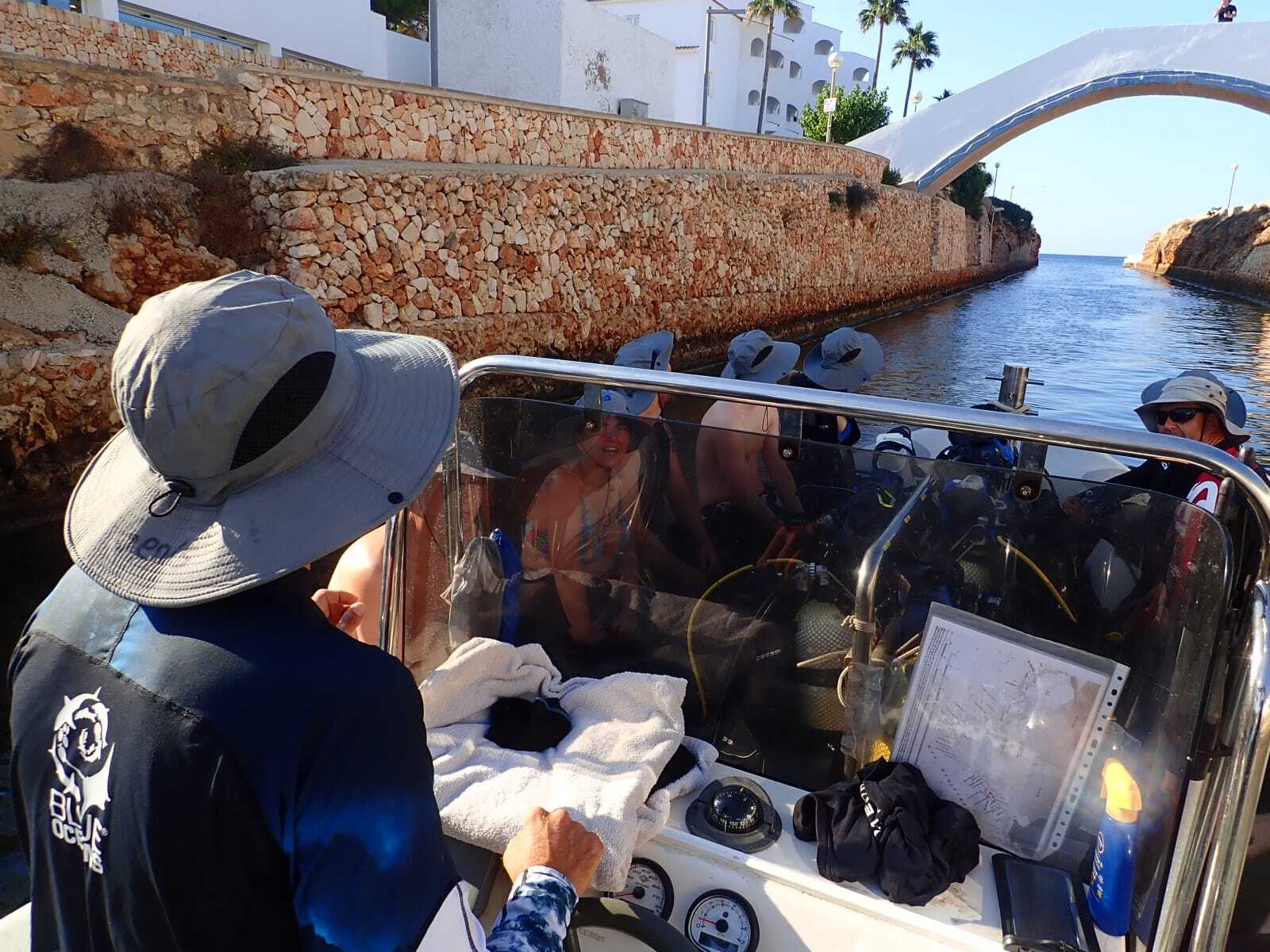 Barca da immersione che percorre un canale costiero stretto vicino a Minorca con l'equipaggio a bordo