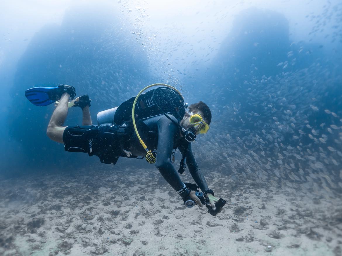 Subacqueo tra un banco di pesci nelle acque blu profonde al largo di Minorca