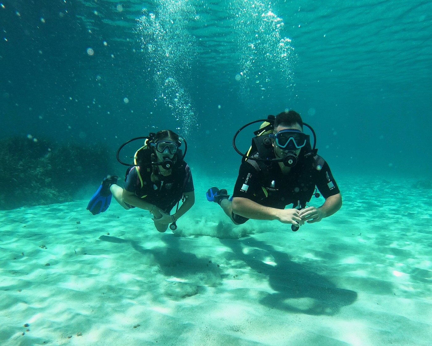Two scuba divers exploring the sandy seabed in clear turquoise waters off Menorca