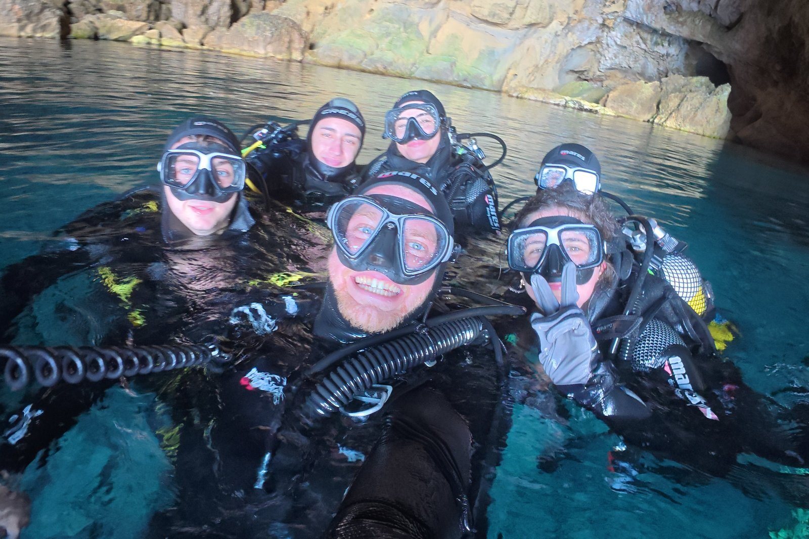 Un gruppo di subacquei di Buceo Cabo La Nao, sorridenti, galleggia insieme in una cala turchese della Costa Blanca
