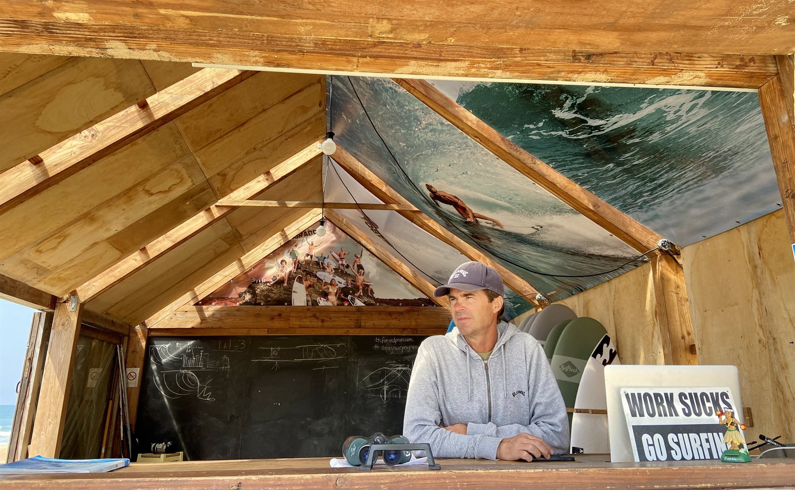 Il coach di surf Didier Piter alla sua scrivania rustica sulla spiaggia di Hossegor con una lavagna e un binocolo
