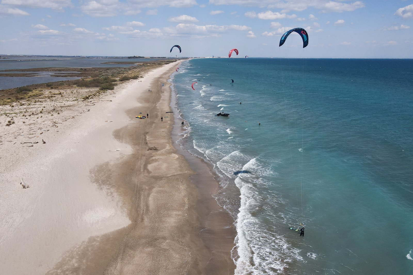 Veduta aerea di kitesurfisti sull’acqua turchese lungo la lunga lingua di sabbia vicino a Montpellier, con gli aquiloni in cielo