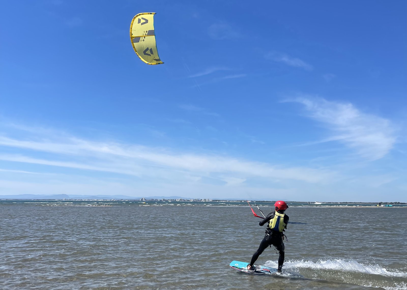 Un rider di Seb Garat Ride Academy scivola su acqua chiara e poco profonda sotto un aquilone giallo