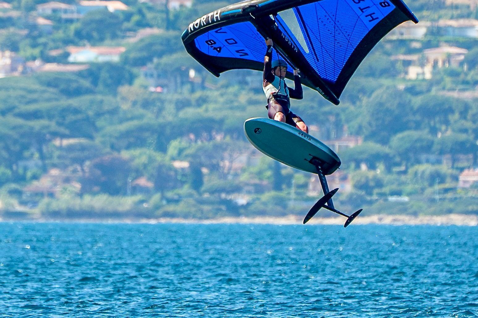 Un wingfoiler stacca dall’acqua con la tavola in alto sopra la baia di Saint-Tropez