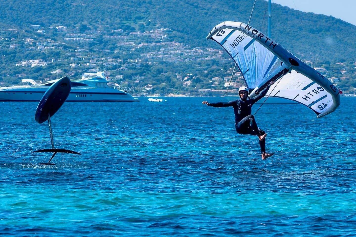 Un wingfoiler salta sopra la baia turchese di Saint-Tropez, con uno yacht di lusso all’ancora sullo sfondo