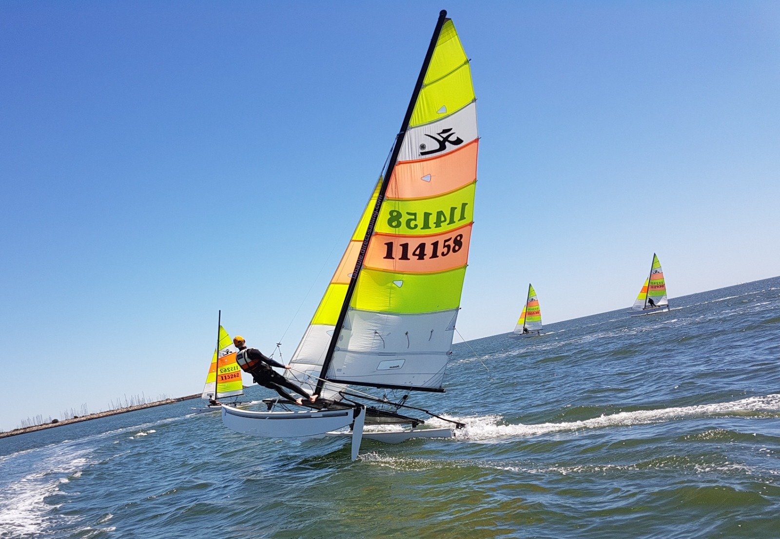 Un velista in regata con un catamarano Hobie Cat colorato al largo della base Yagga